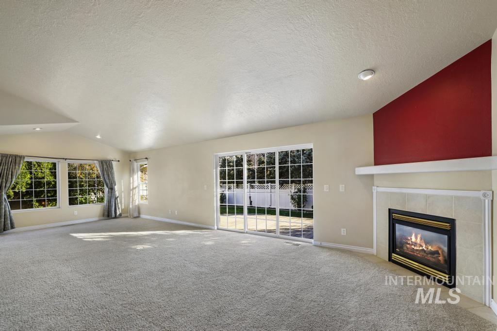Unfurnished living room featuring vaulted ceiling, a textured ceiling, carpet floors, and a tiled fireplace