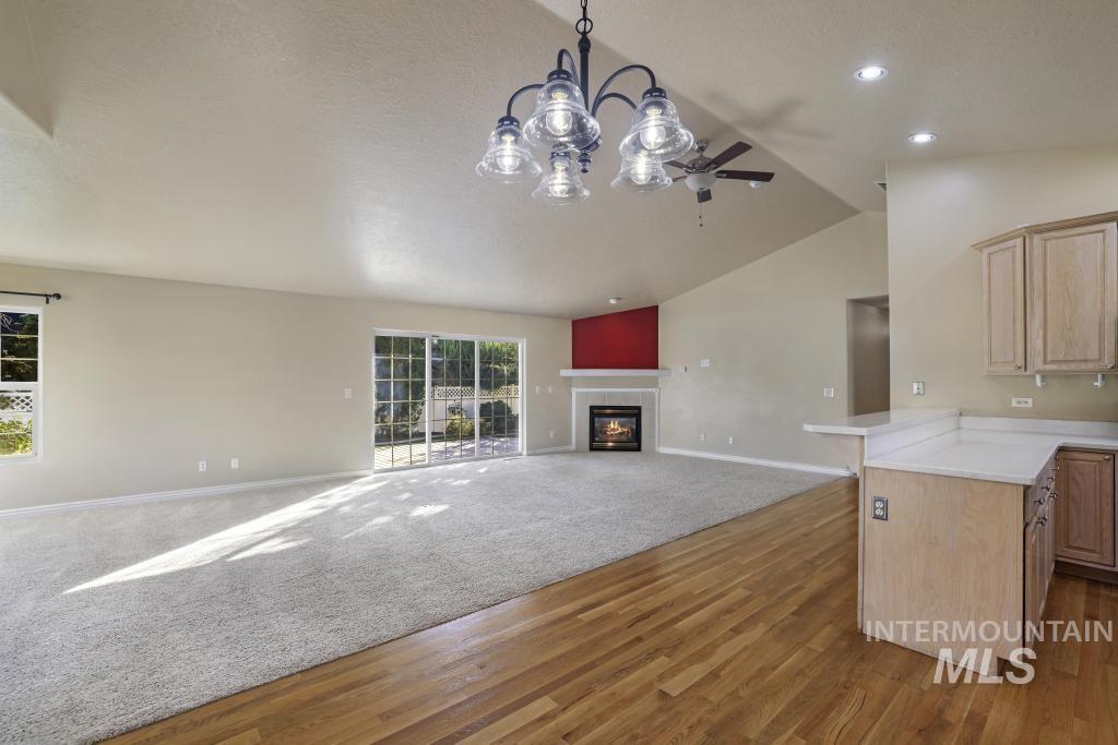 Unfurnished living room featuring vaulted ceiling, a fireplace, a chandelier, light wood-style floors, and ceiling fan