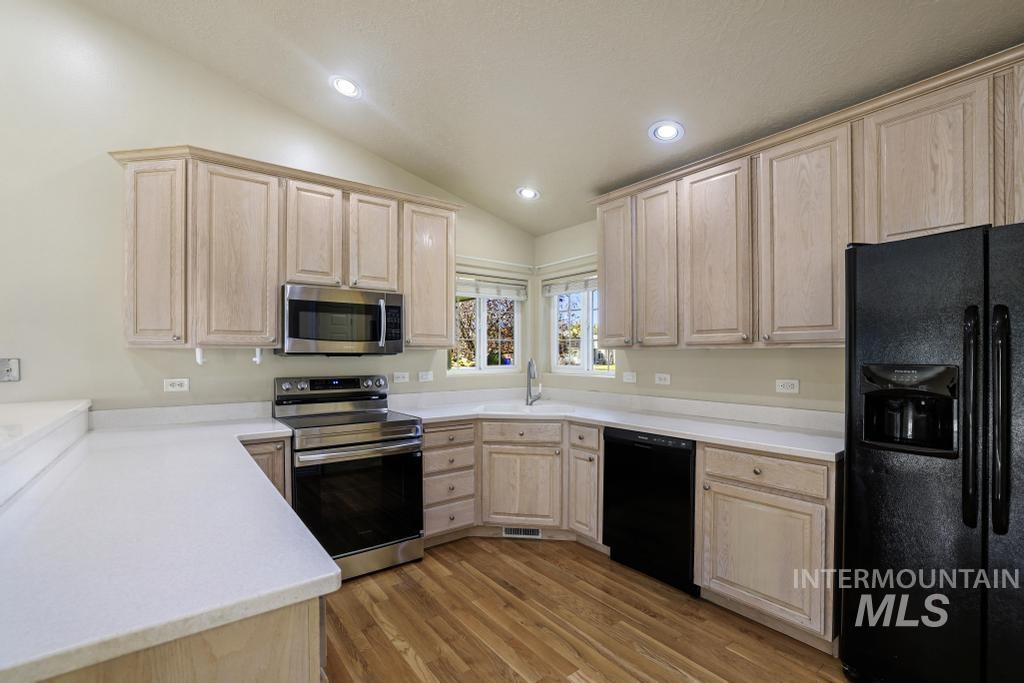 Kitchen featuring light brown cabinets, vaulted ceiling, black appliances, light wood finished floors, and recessed lighting