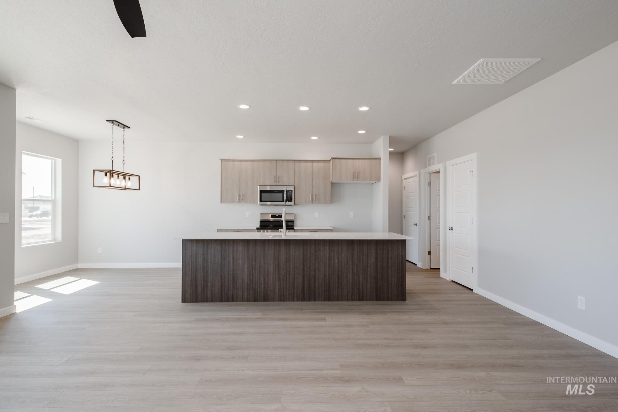 Kitchen with a center island with sink, modern cabinets, light wood-style flooring, hanging light fixtures, and appliances with stainless steel finishes
