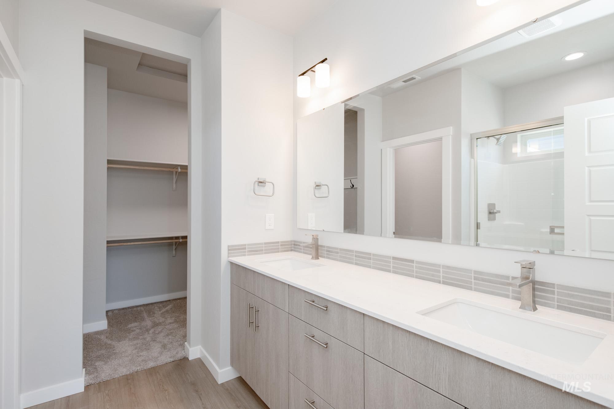 Bathroom with light wood-type flooring, a stall shower, double vanity, and a spacious closet