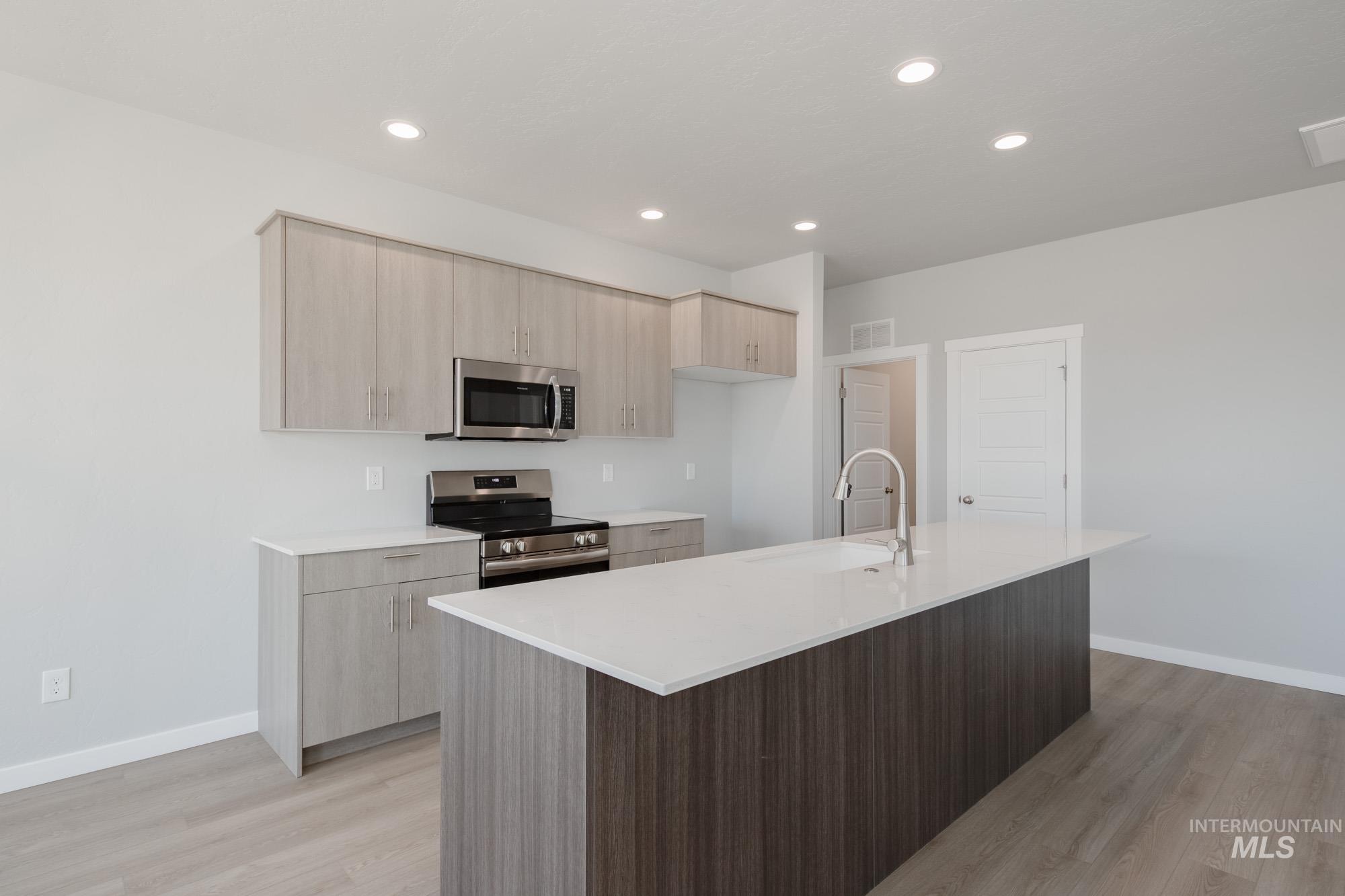 Kitchen featuring light brown cabinetry, modern cabinets, stainless steel appliances, light stone countertops, and a kitchen island with sink