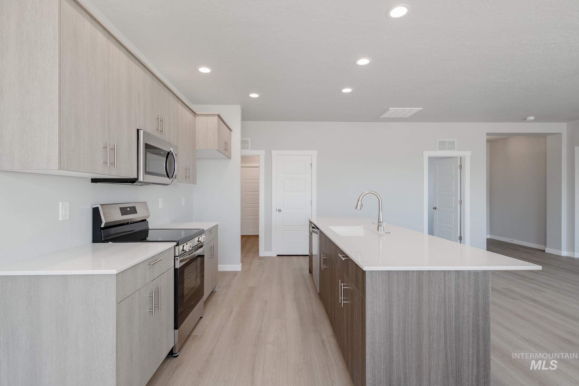 Kitchen featuring stainless steel appliances, modern cabinets, light wood-style floors, recessed lighting, and a center island with sink