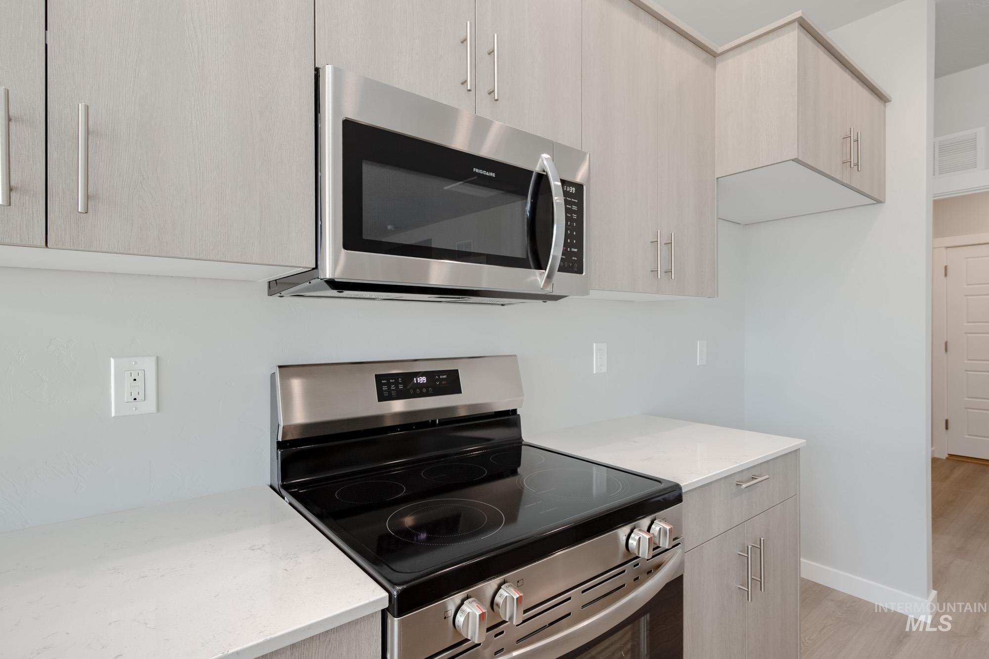 Kitchen featuring stainless steel appliances, modern cabinets, light stone counters, light wood-type flooring, and light brown cabinetry