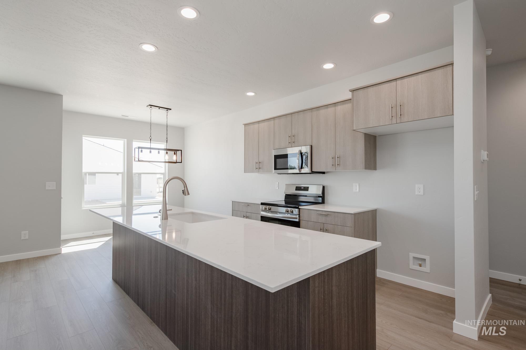 Kitchen with light stone counters, an island with sink, stainless steel appliances, light brown cabinets, and recessed lighting
