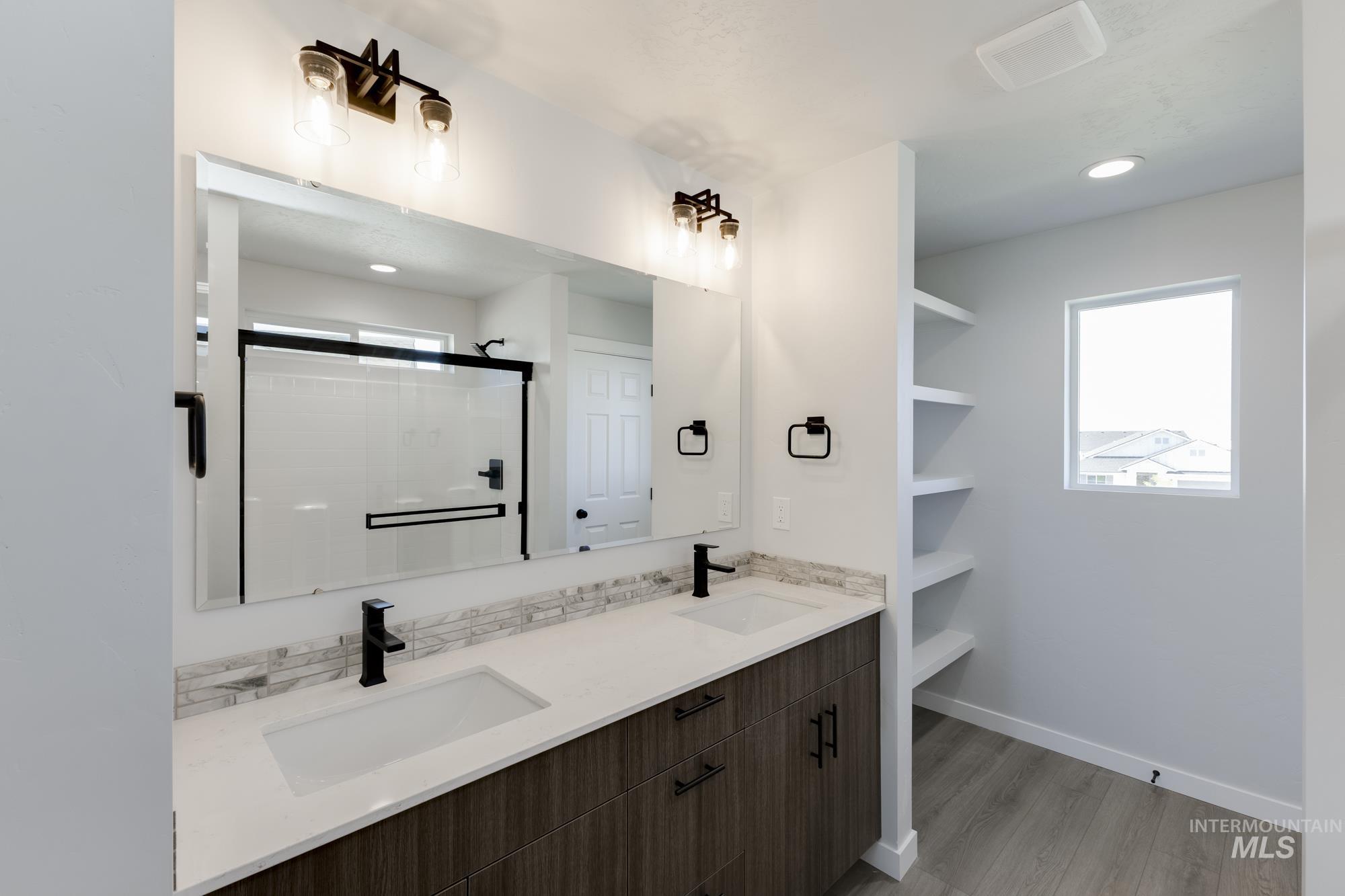Bathroom featuring double vanity, light wood-type flooring, healthy amount of natural light, a shower stall, and recessed lighting