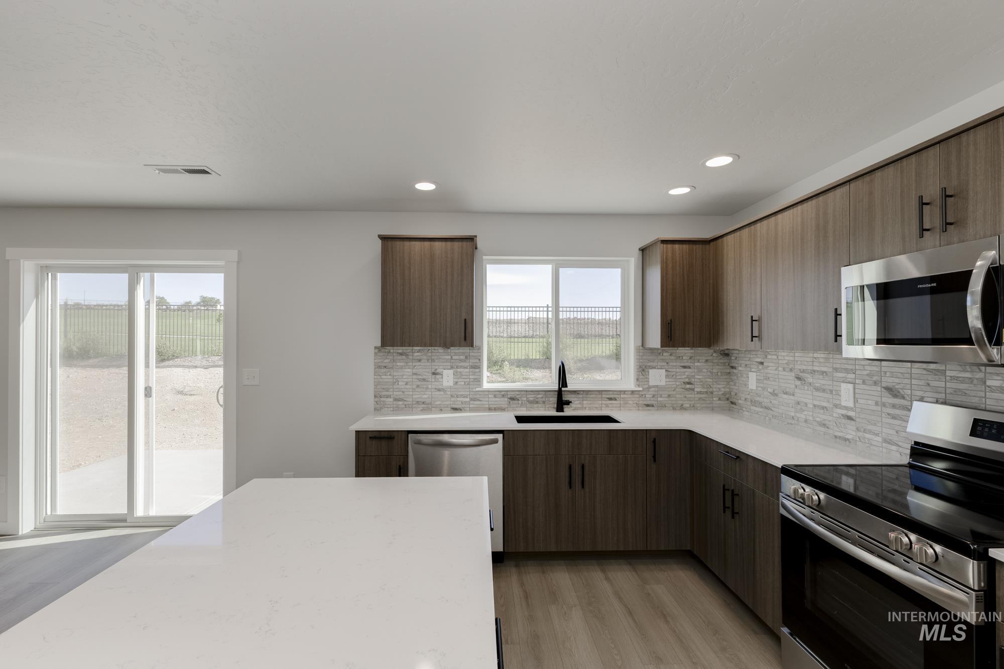 Kitchen featuring appliances with stainless steel finishes, light wood-style floors, decorative backsplash, light stone counters, and recessed lighting