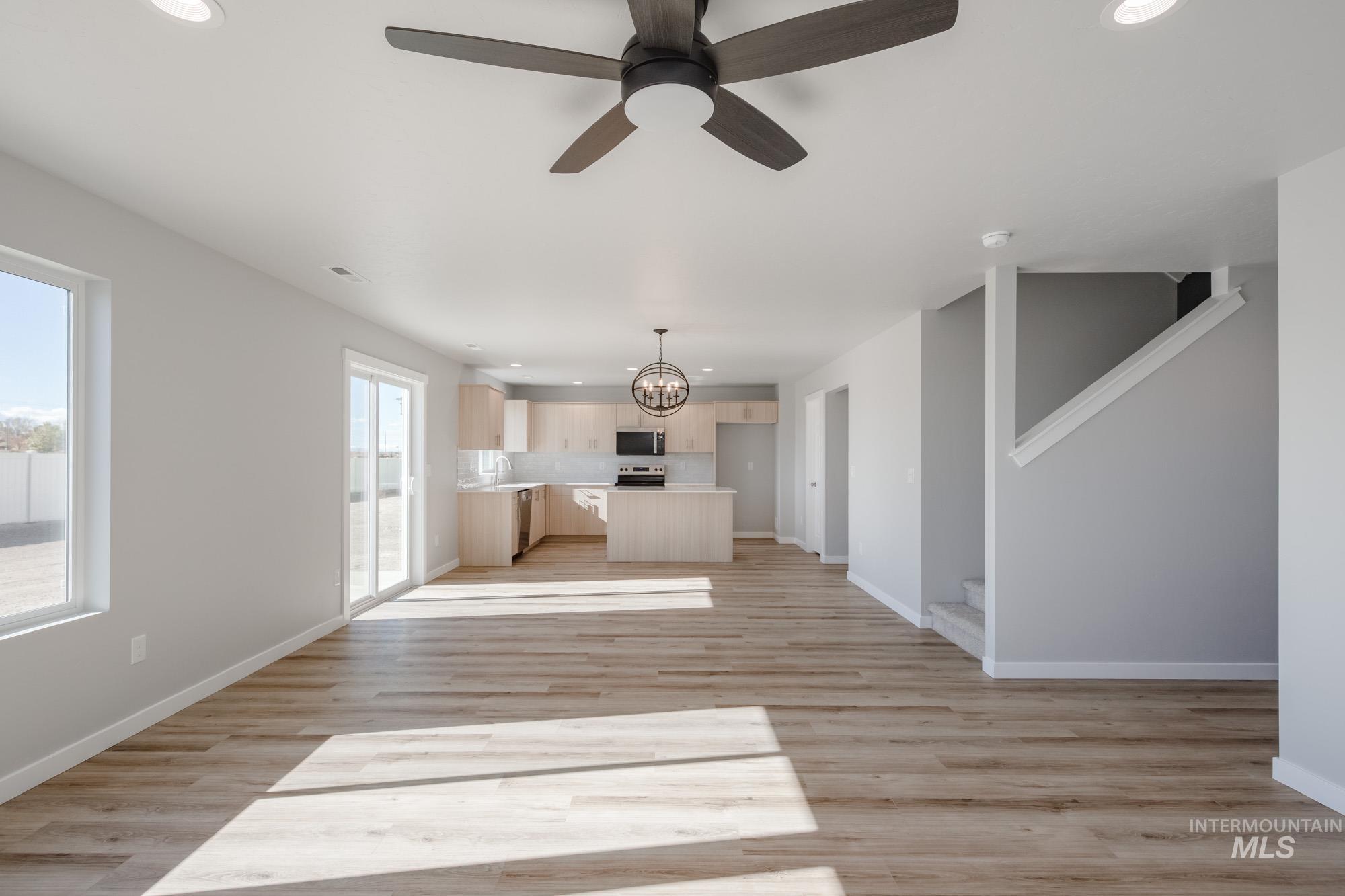 Unfurnished living room with recessed lighting, light wood-style floors, a chandelier, a ceiling fan, and stairs
