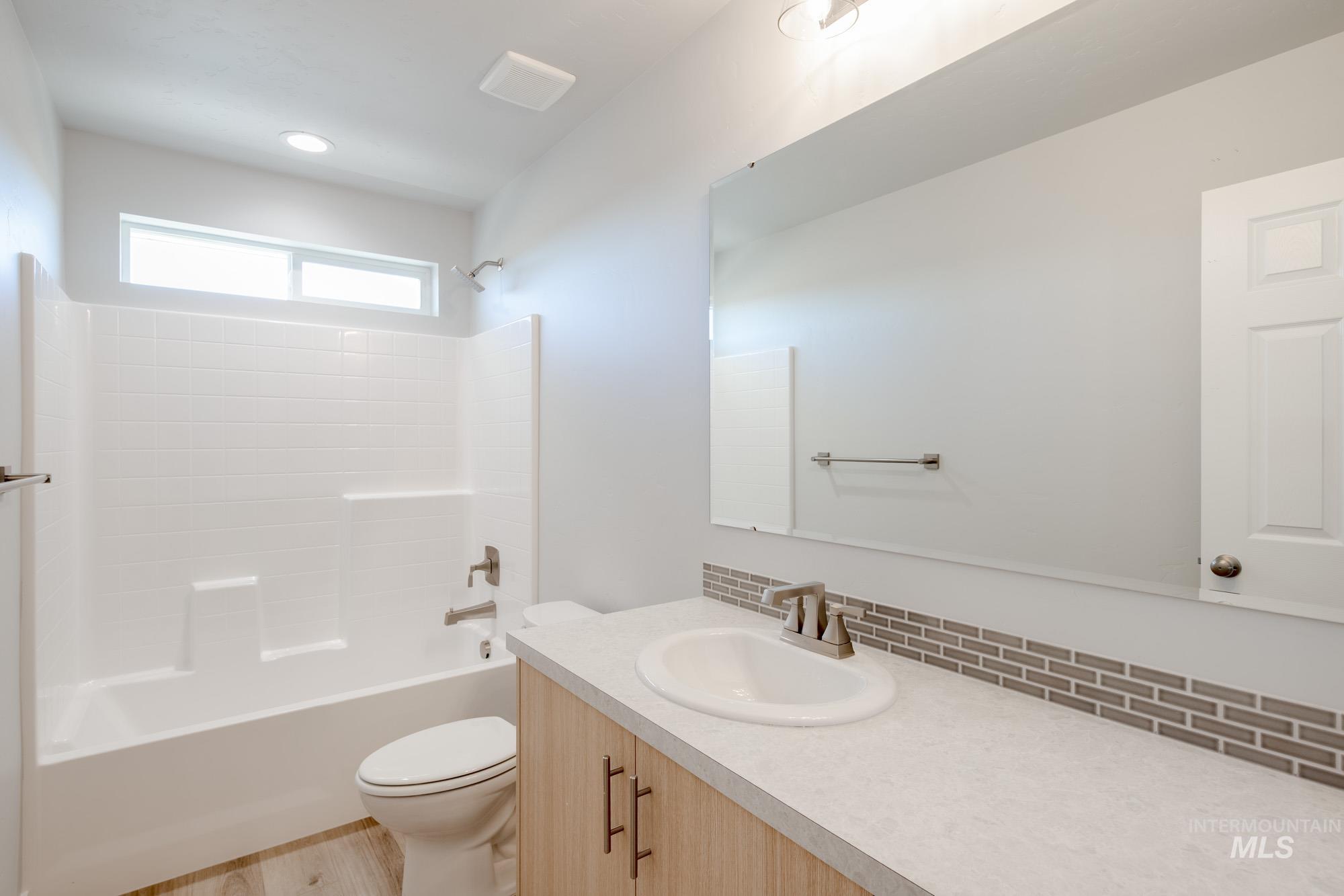 Bathroom featuring bathing tub / shower combination, vanity, tasteful backsplash, and light wood-style floors
