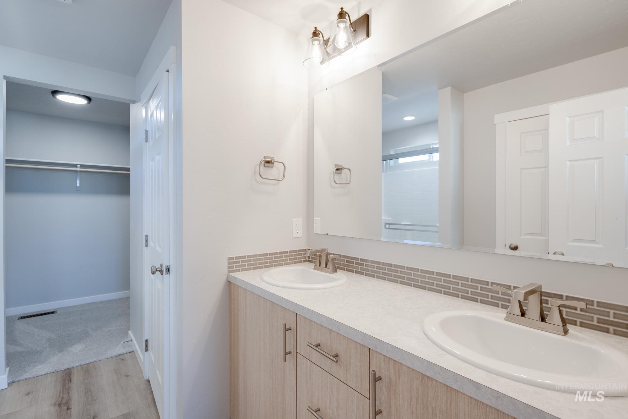 Bathroom featuring light wood-type flooring, double vanity, a spacious closet, tasteful backsplash, and a shower stall