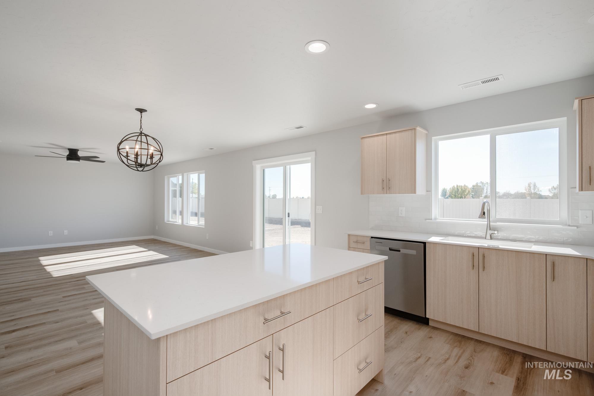 Kitchen with light brown cabinetry, light wood-style flooring, a center island, a chandelier, and pendant lighting