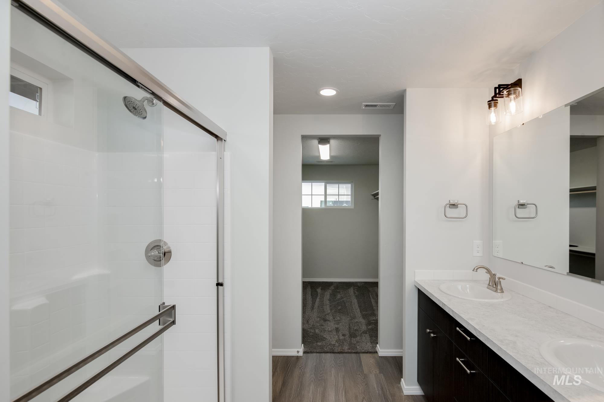 Bathroom with a stall shower, dark wood-type flooring, double vanity, and recessed lighting