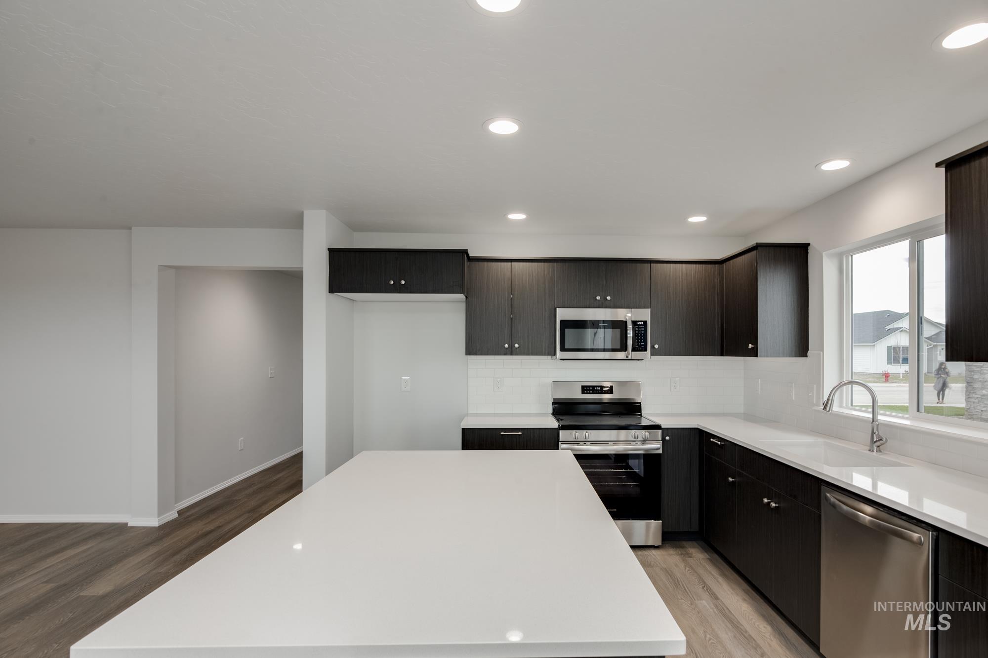 Kitchen with stainless steel appliances, light wood-style flooring, recessed lighting, light stone countertops, and backsplash