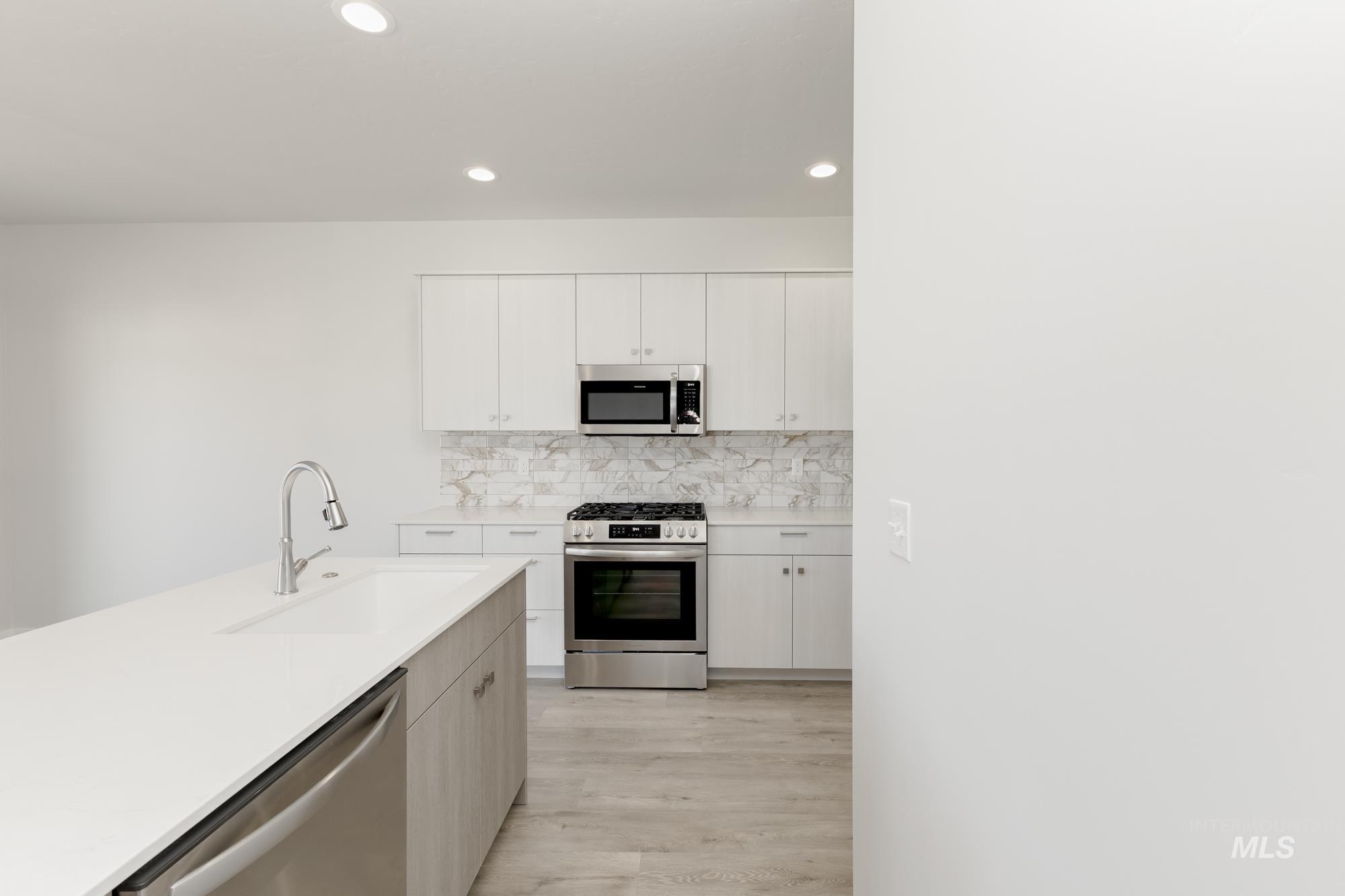 Kitchen featuring appliances with stainless steel finishes, decorative backsplash, recessed lighting, light wood finished floors, and white cabinetry