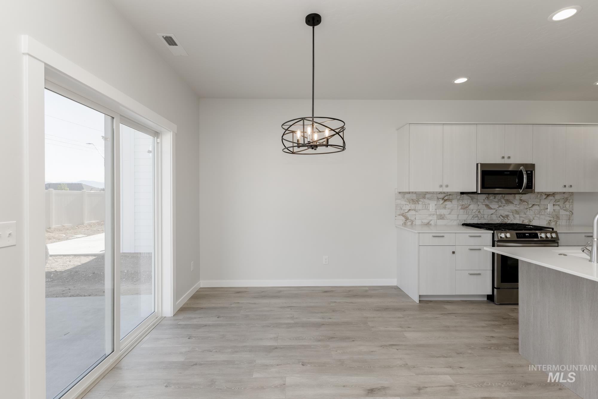 Kitchen with appliances with stainless steel finishes, decorative light fixtures, white cabinets, a chandelier, and decorative backsplash