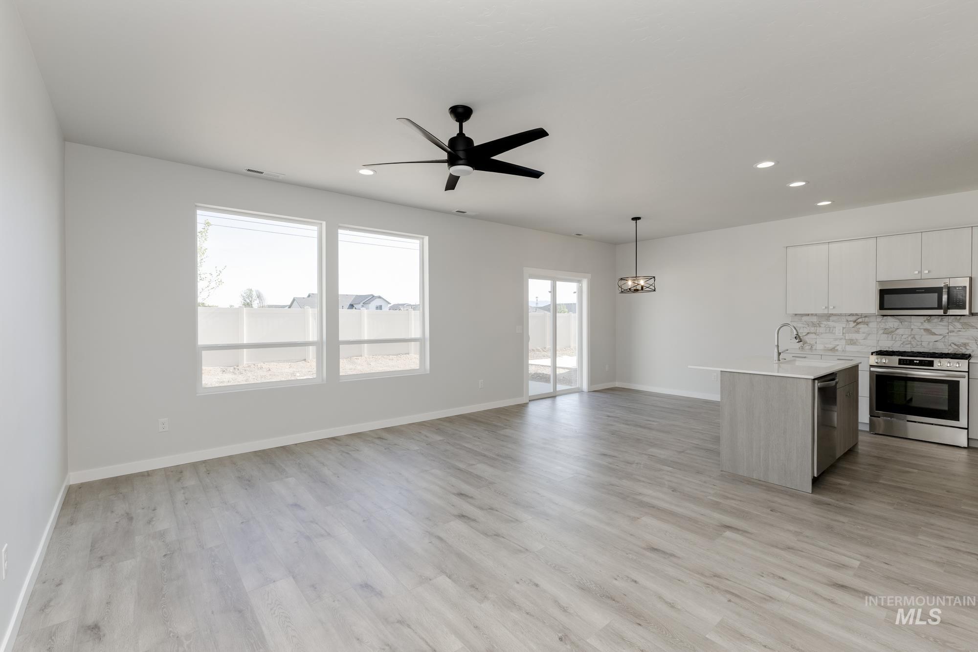 Kitchen featuring stainless steel appliances, decorative backsplash, open floor plan, an island with sink, and decorative light fixtures