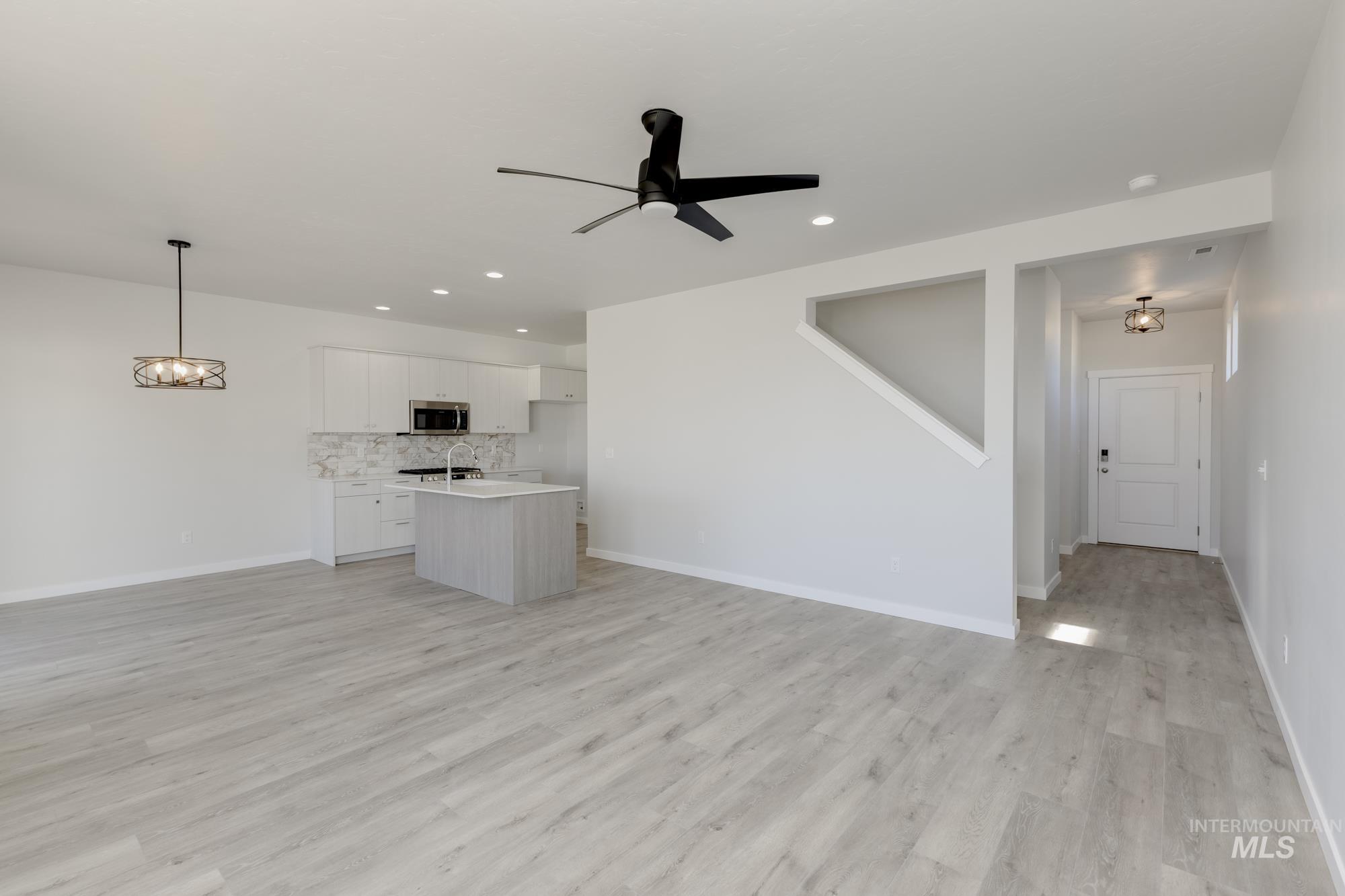 Unfurnished living room featuring light wood-style flooring, a ceiling fan, recessed lighting, and a chandelier