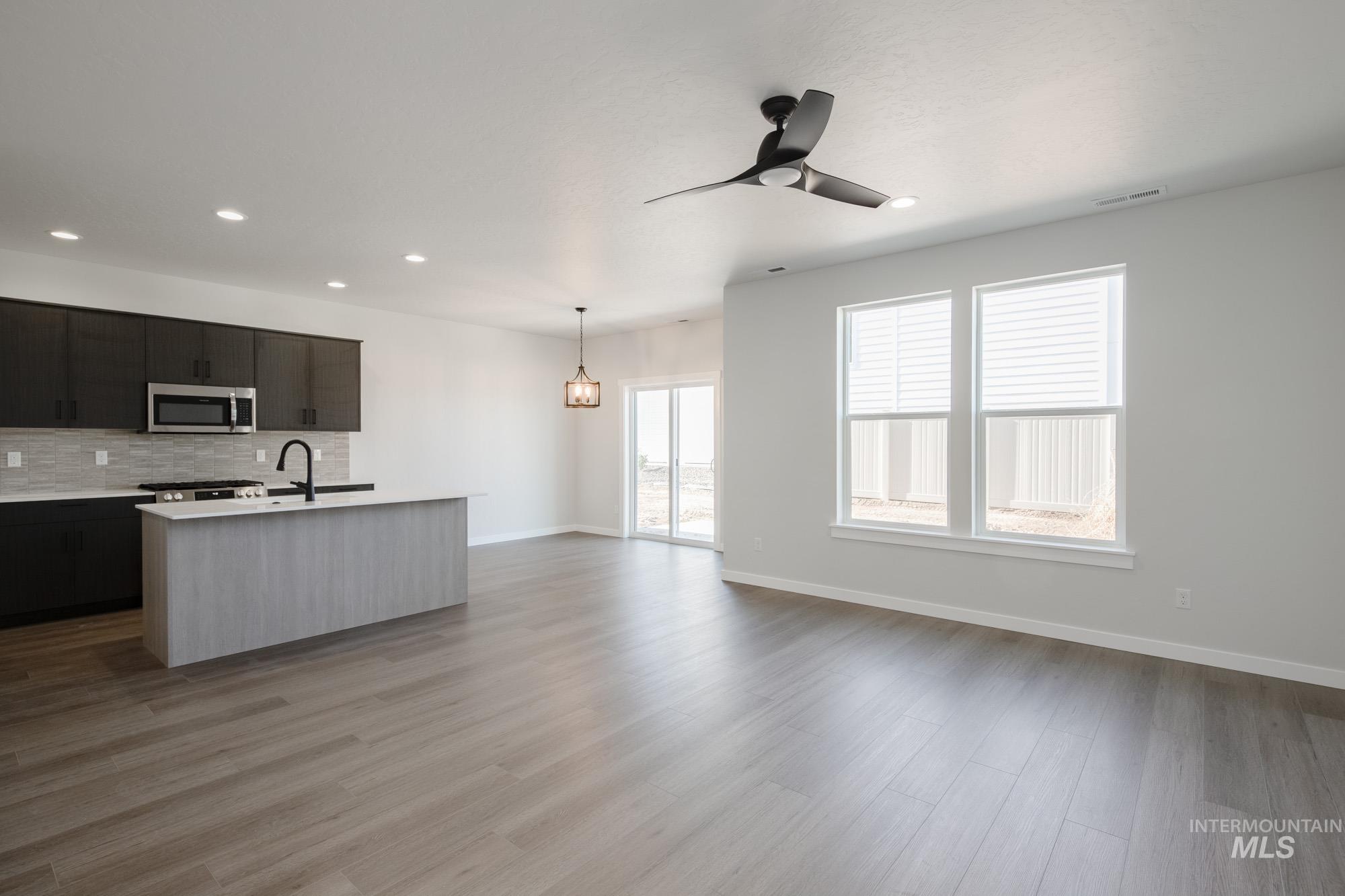 Kitchen with open floor plan, hanging light fixtures, tasteful backsplash, a center island with sink, and stainless steel microwave