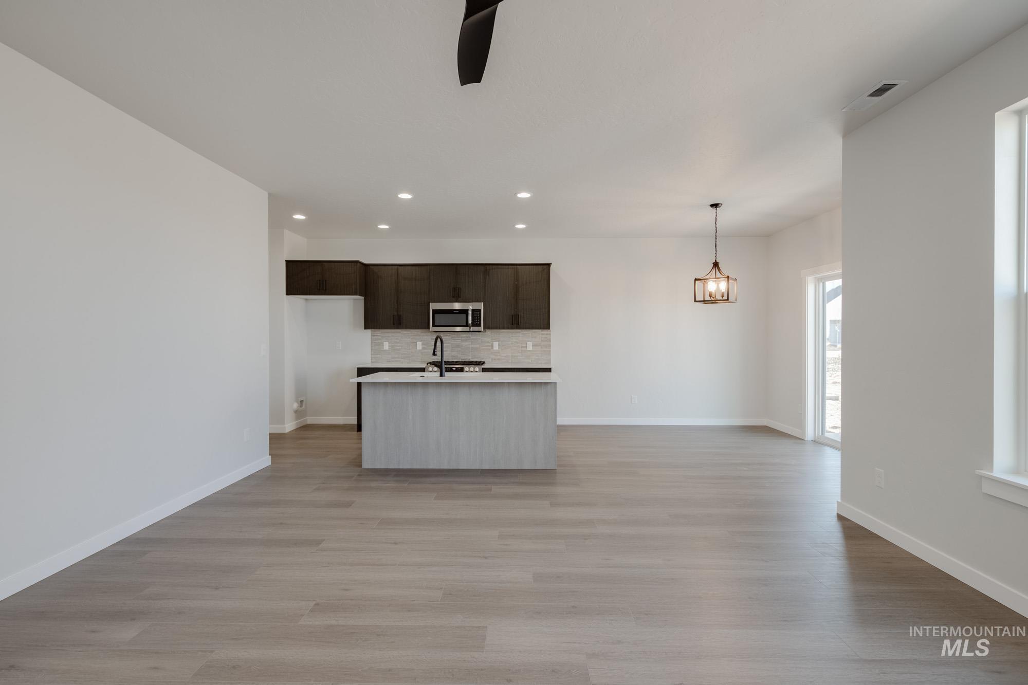 Kitchen with light countertops, an island with sink, light wood-style flooring, open floor plan, and decorative backsplash