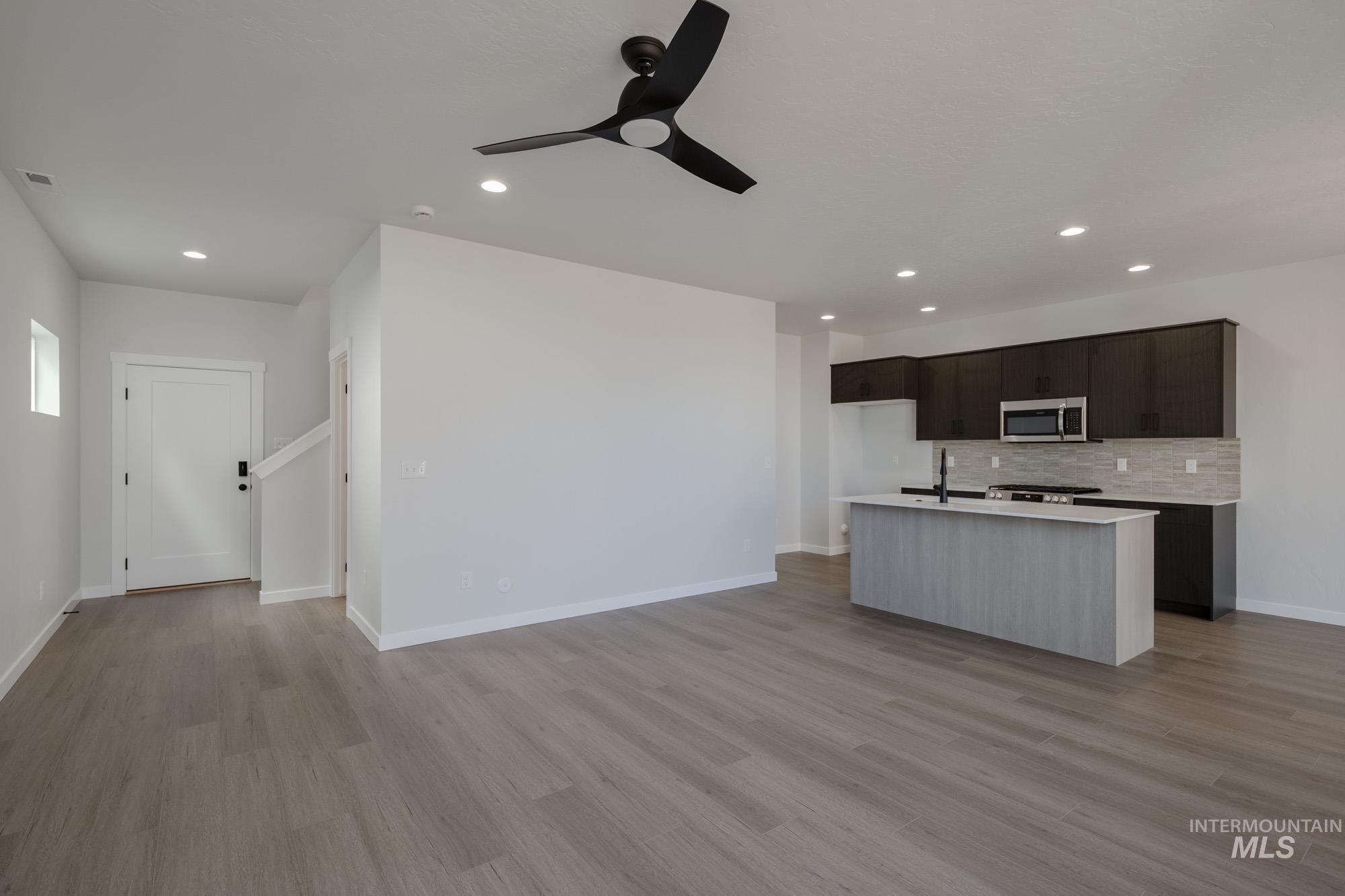 Kitchen with open floor plan, a kitchen island with sink, decorative backsplash, recessed lighting, and light wood-style floors