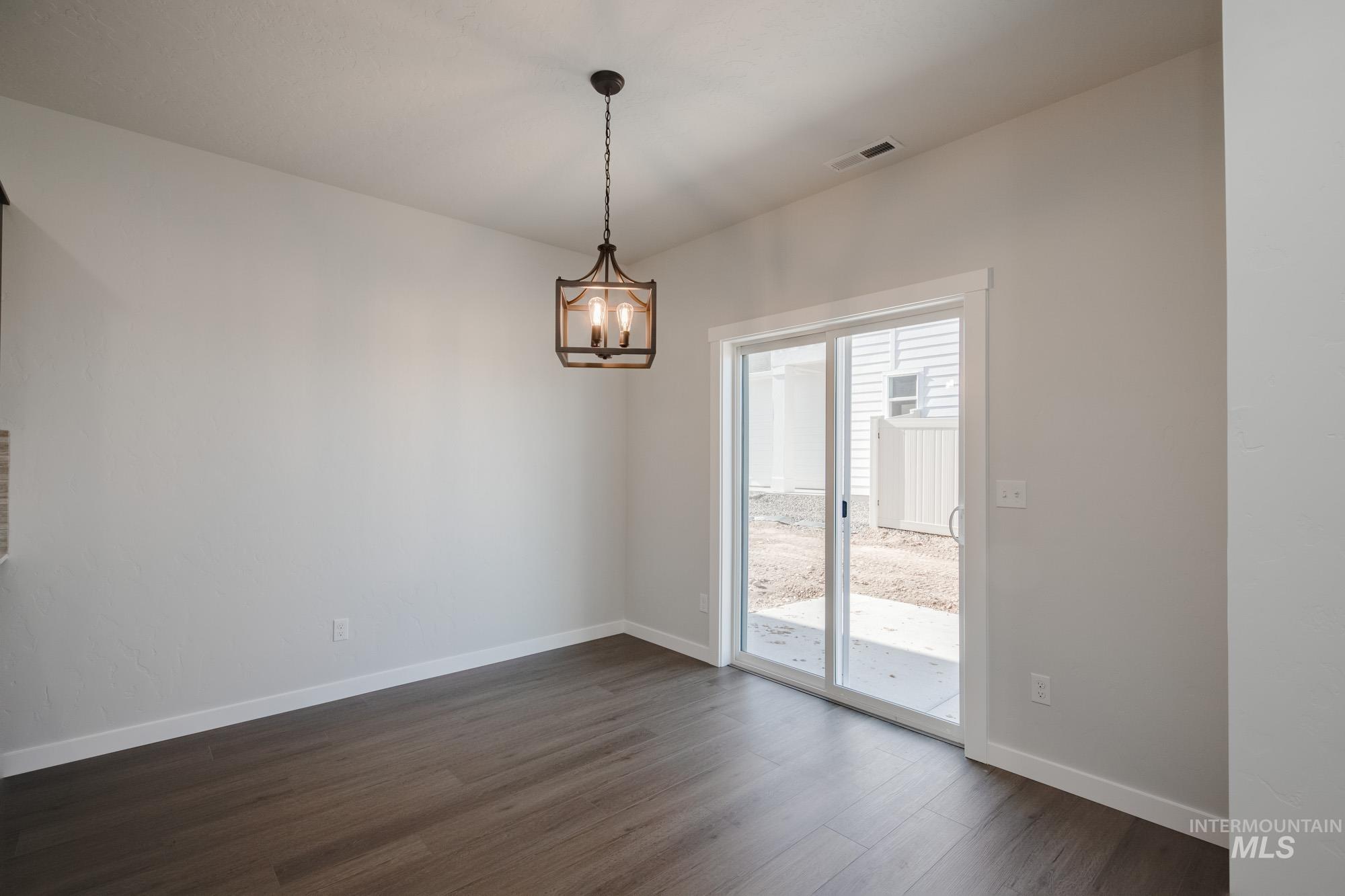 Empty room with dark wood finished floors and a chandelier