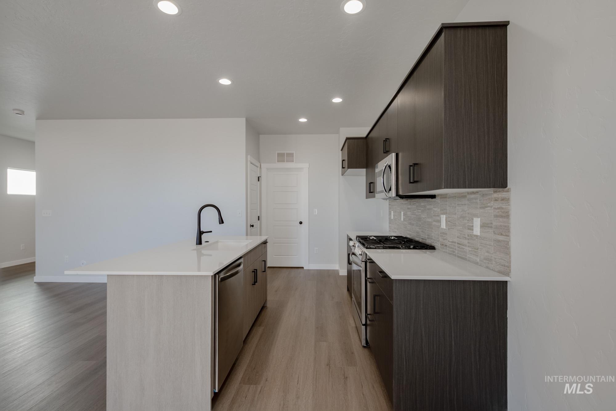Kitchen featuring appliances with stainless steel finishes, modern cabinets, a kitchen island with sink, light stone countertops, and recessed lighting