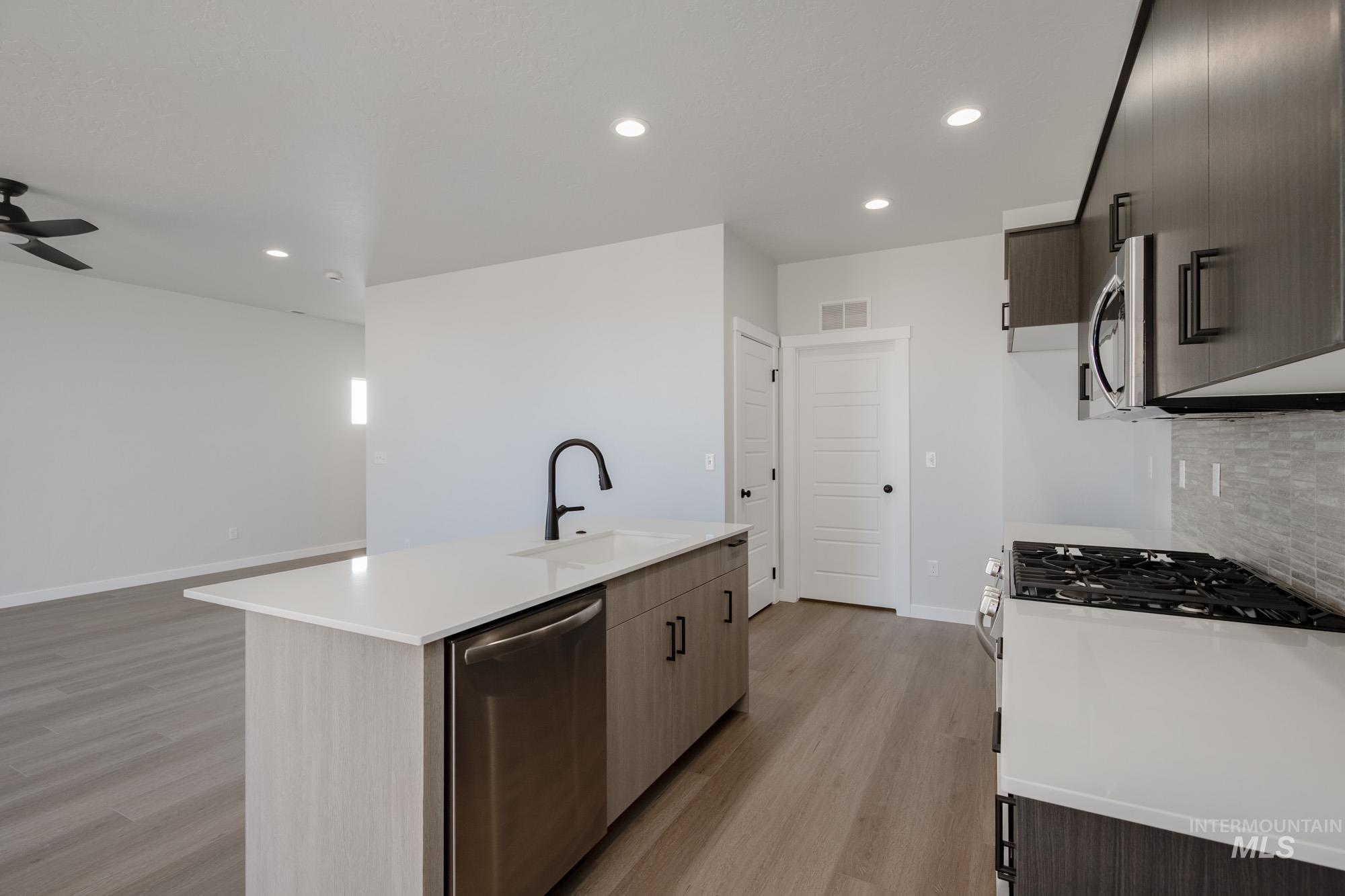 Kitchen with modern cabinets, recessed lighting, appliances with stainless steel finishes, light wood-style flooring, and a kitchen island with sink