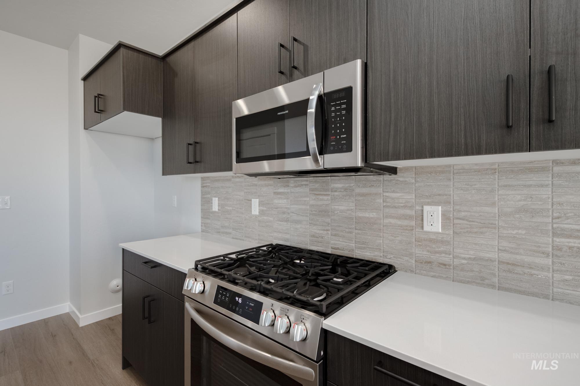Kitchen featuring stainless steel appliances, modern cabinets, light wood-style flooring, decorative backsplash, and dark brown cabinetry