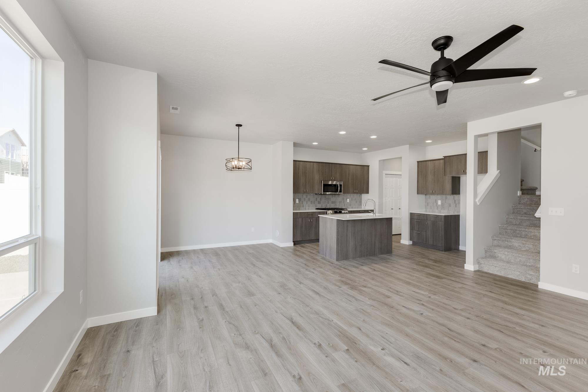 Unfurnished living room featuring a chandelier, light wood-style floors, ceiling fan, stairs, and recessed lighting