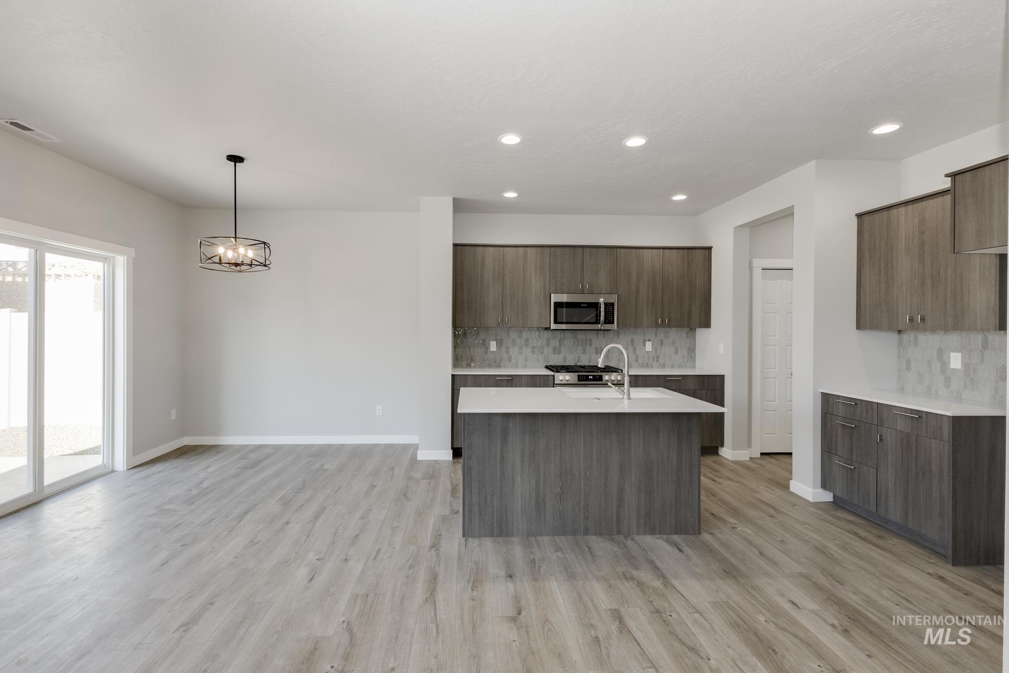 Kitchen with tasteful backsplash, modern cabinets, decorative light fixtures, a center island with sink, and light wood-style flooring