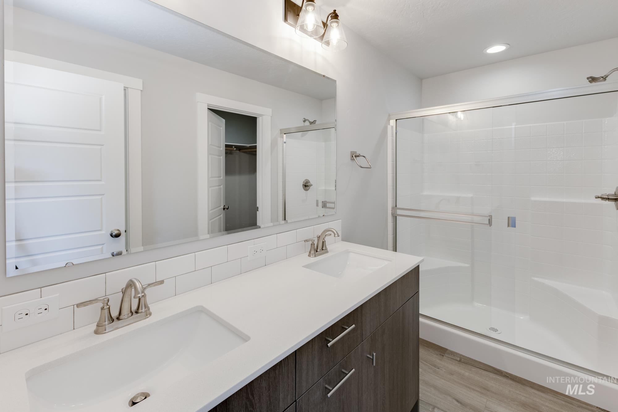 Full bath featuring a shower stall, double vanity, decorative backsplash, light wood-style flooring, and recessed lighting