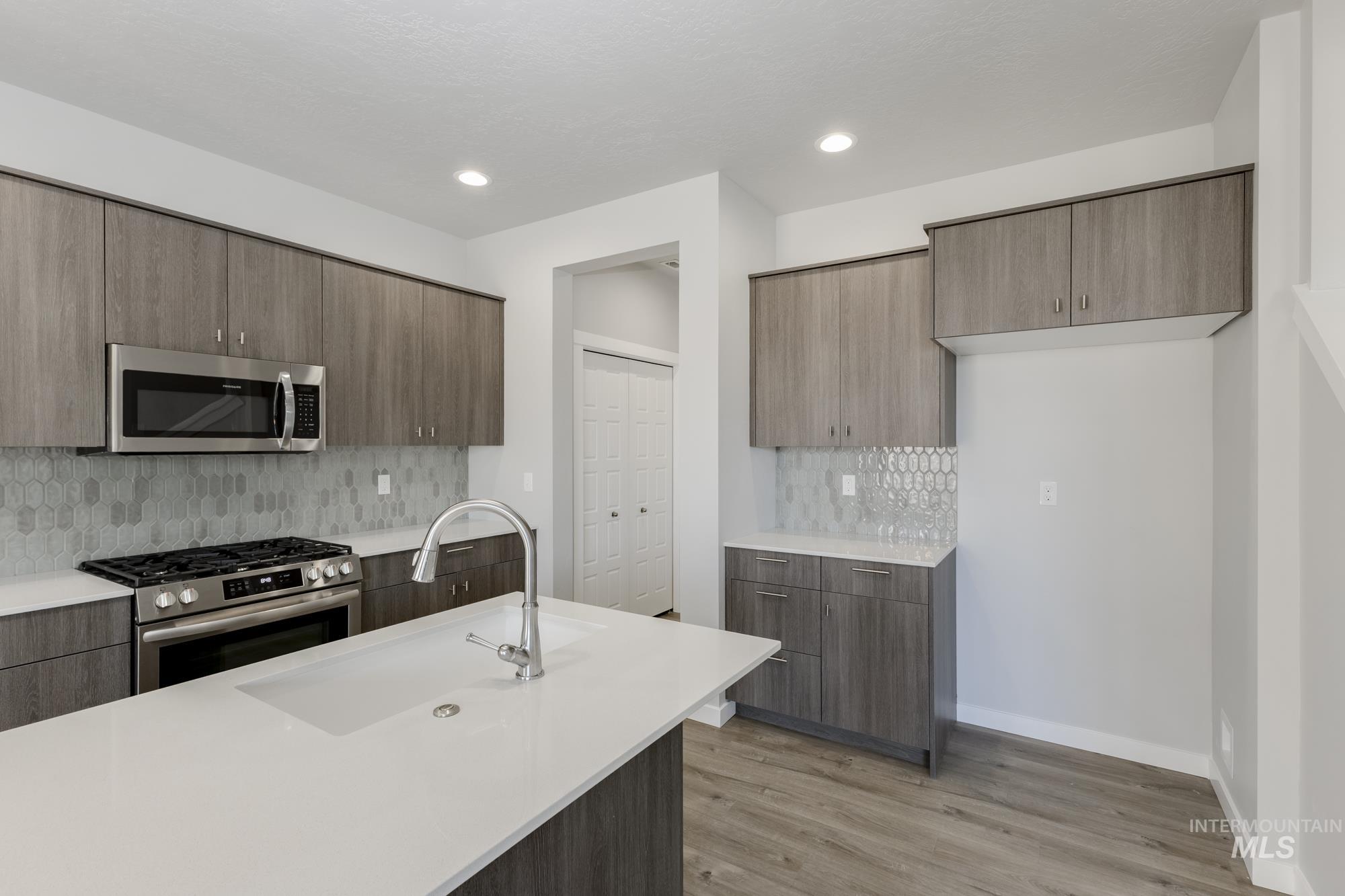Kitchen with appliances with stainless steel finishes, modern cabinets, tasteful backsplash, light wood-type flooring, and recessed lighting