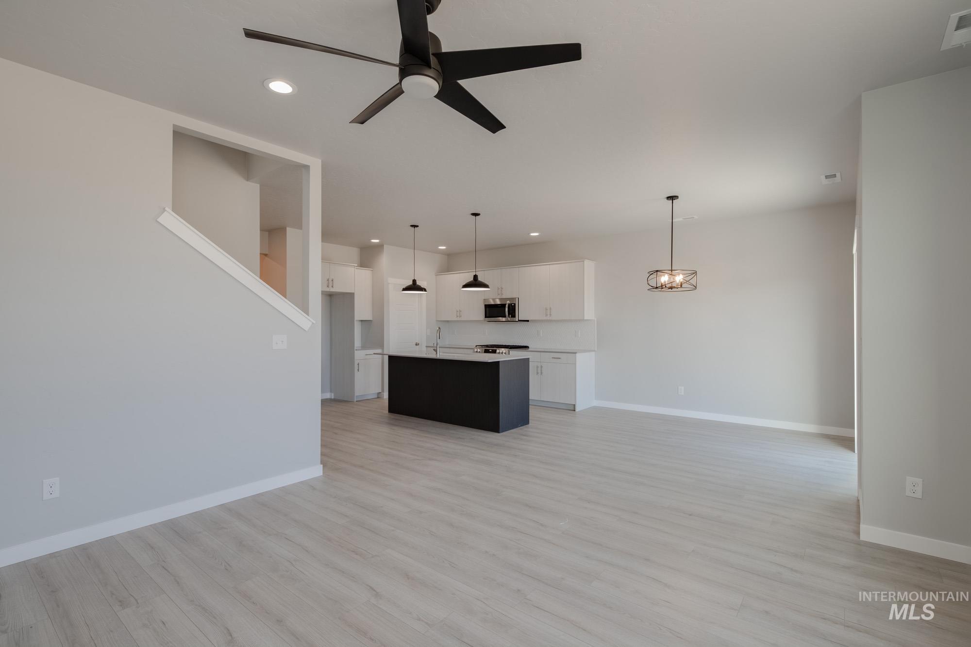 Unfurnished living room featuring light wood-style flooring, recessed lighting, ceiling fan, and a chandelier