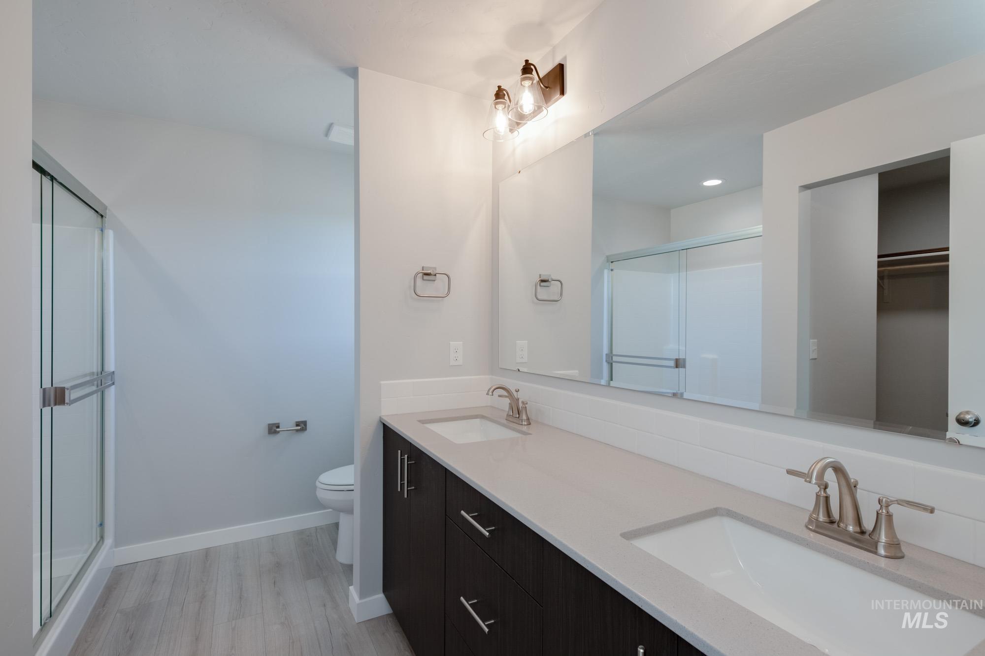 Full bath with double vanity, light wood-style floors, a stall shower, and a spacious closet
