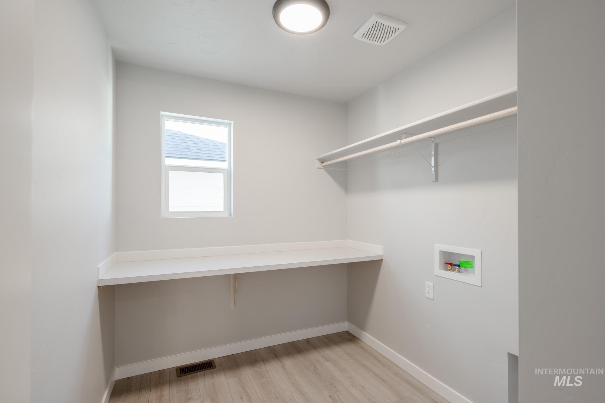 Washroom with hookup for a washing machine and light wood-style flooring