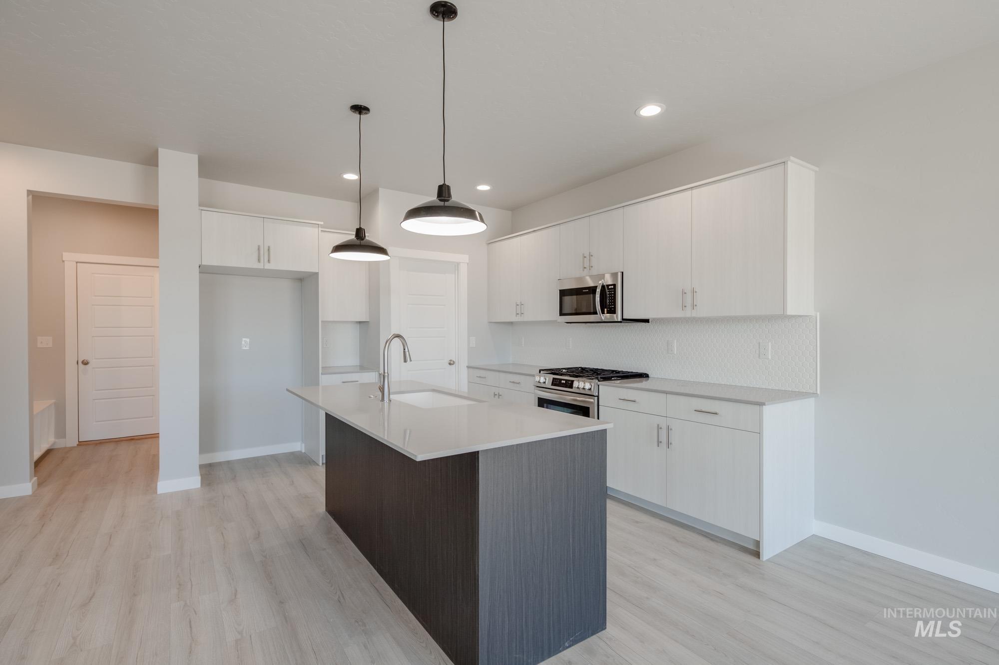Kitchen with stainless steel appliances, hanging light fixtures, white cabinets, a center island with sink, and recessed lighting