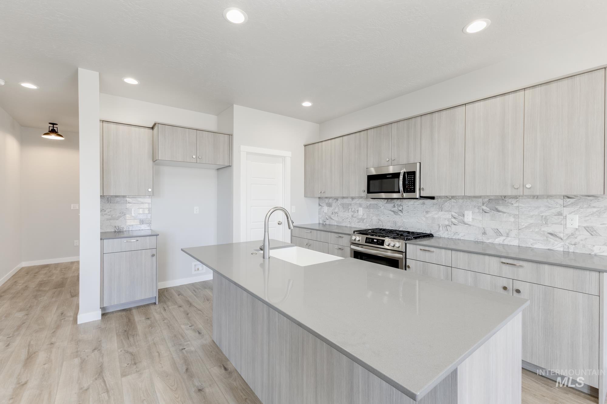 Kitchen featuring backsplash, modern cabinets, stainless steel appliances, light stone counters, and light wood finished floors