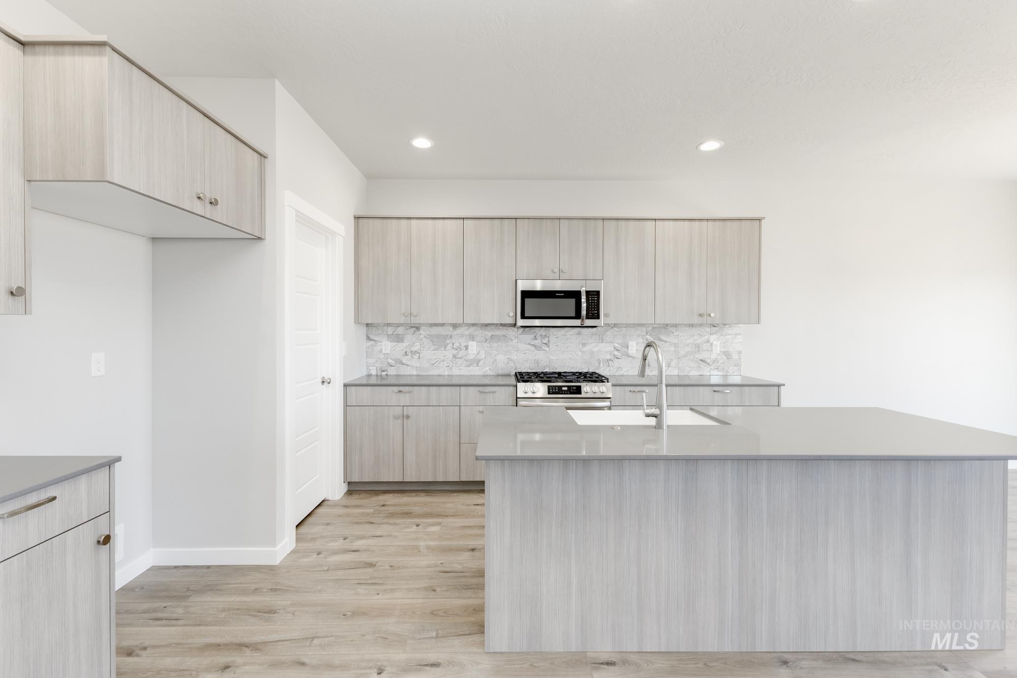 Kitchen with backsplash, stainless steel appliances, light wood finished floors, a kitchen island with sink, and light stone counters