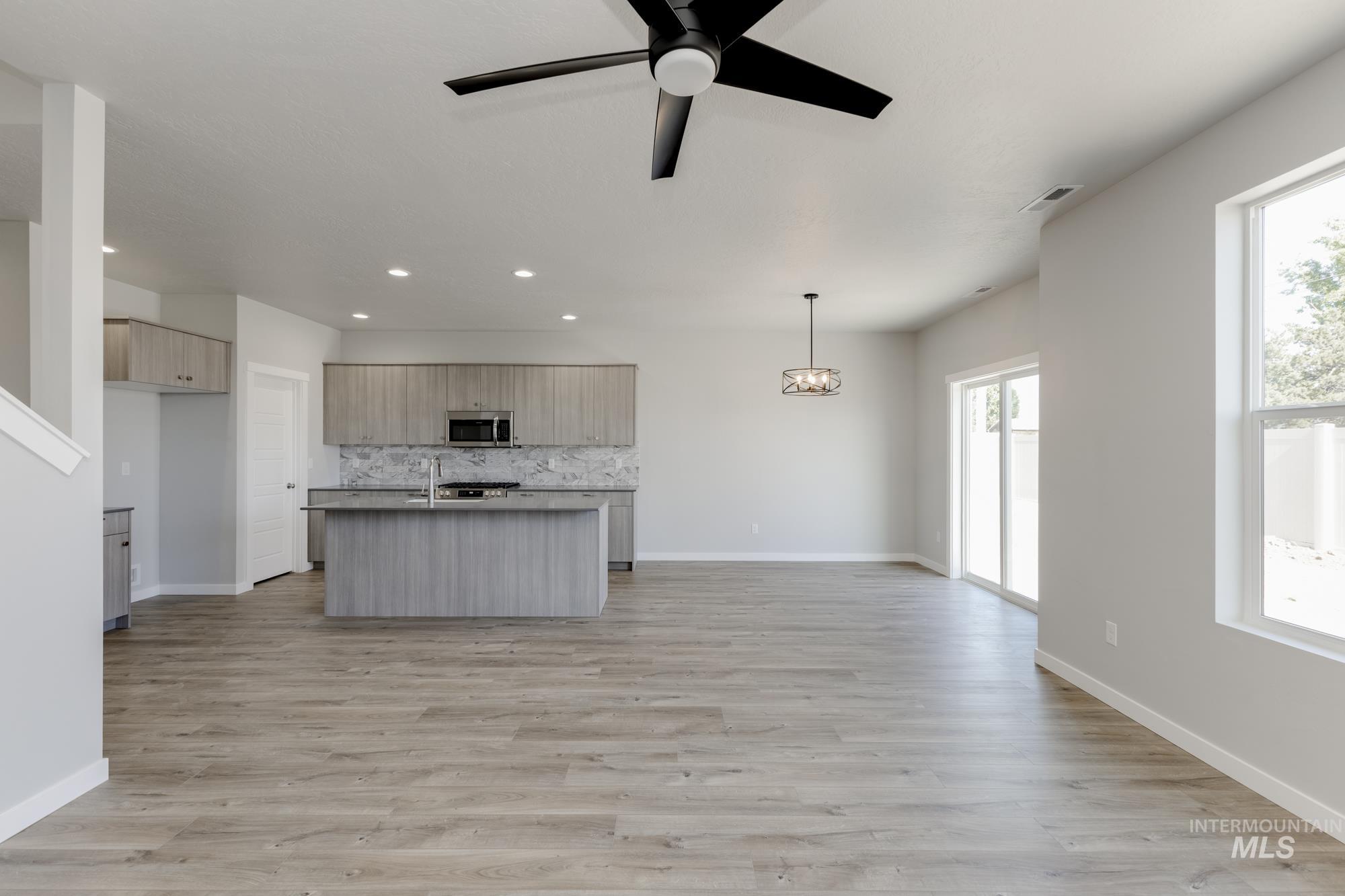 Kitchen with open floor plan, a center island with sink, light wood-style flooring, modern cabinets, and a ceiling fan