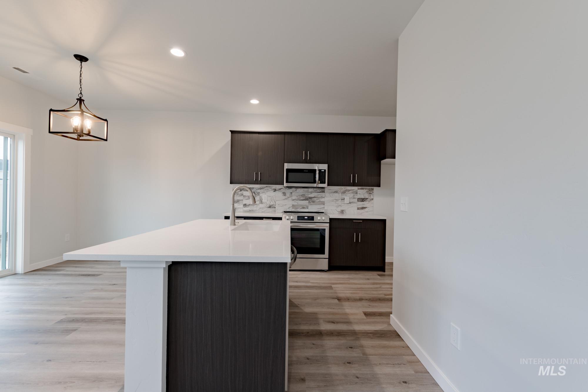 Kitchen featuring backsplash, appliances with stainless steel finishes, a kitchen island with sink, pendant lighting, and recessed lighting