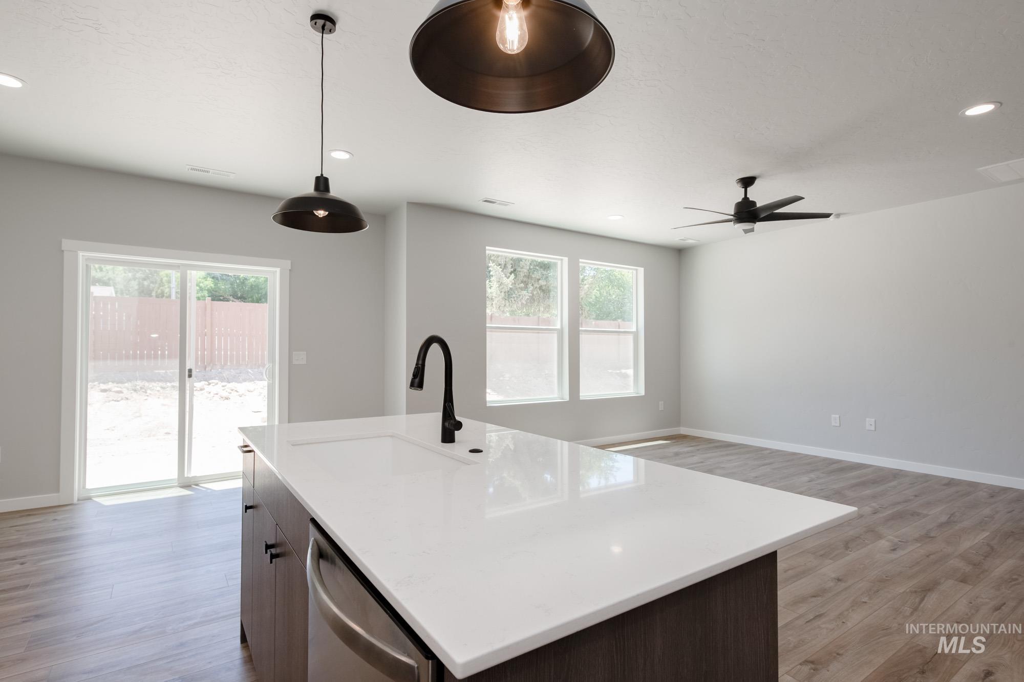 Kitchen with decorative light fixtures, light wood-type flooring, a kitchen island with sink, recessed lighting, and stainless steel dishwasher