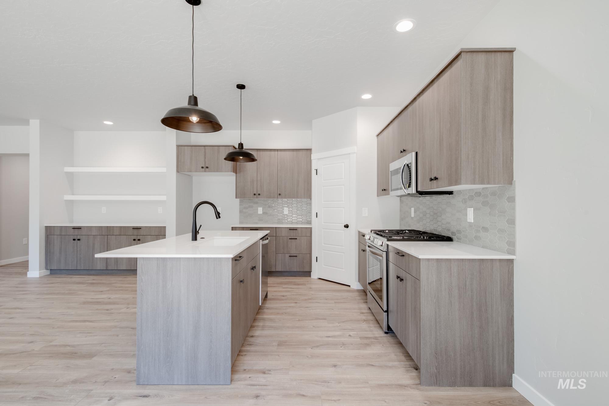 Kitchen with stainless steel appliances, light stone counters, an island with sink, pendant lighting, and modern cabinets