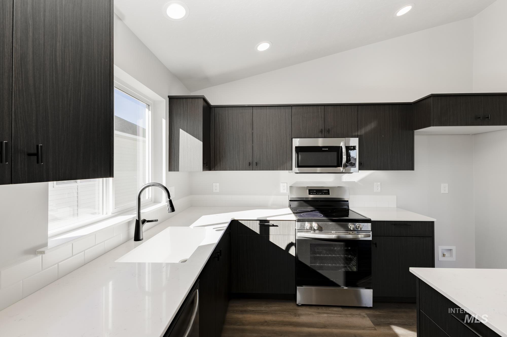 Kitchen featuring appliances with stainless steel finishes, vaulted ceiling, light stone counters, dark wood-type flooring, and modern cabinets