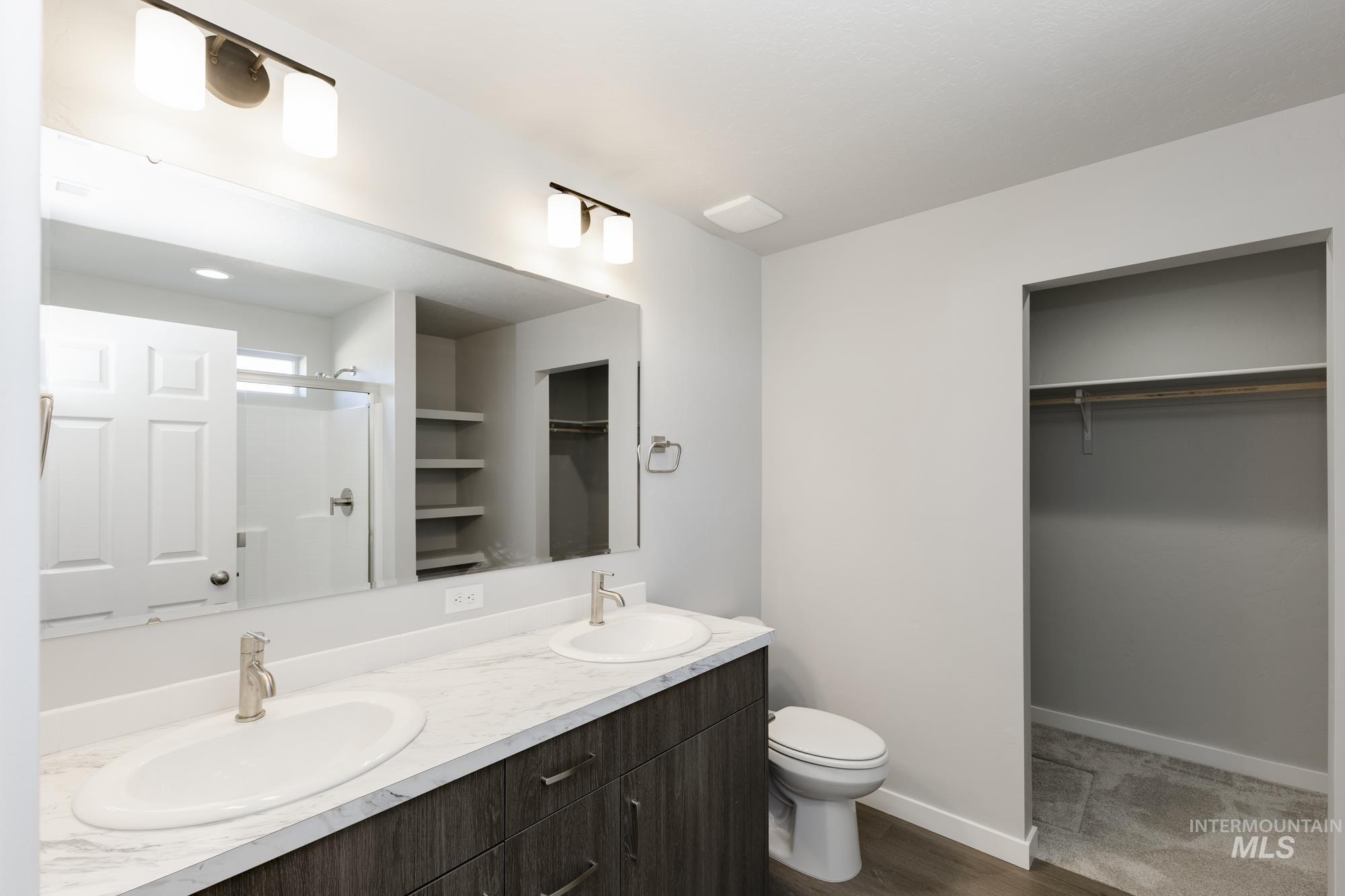 Full bathroom with a spacious closet, a stall shower, double vanity, and dark wood-style floors