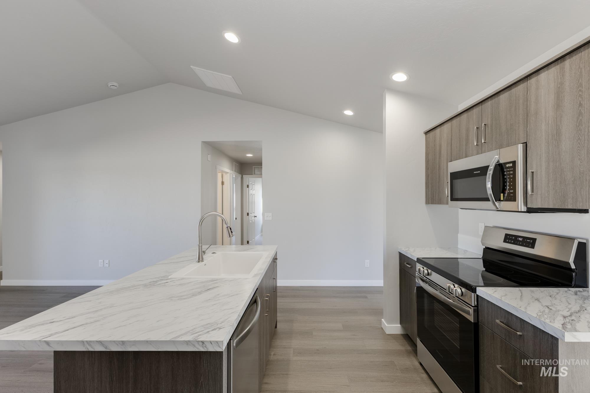 Kitchen with stainless steel appliances, light wood-style floors, recessed lighting, vaulted ceiling, and modern cabinets