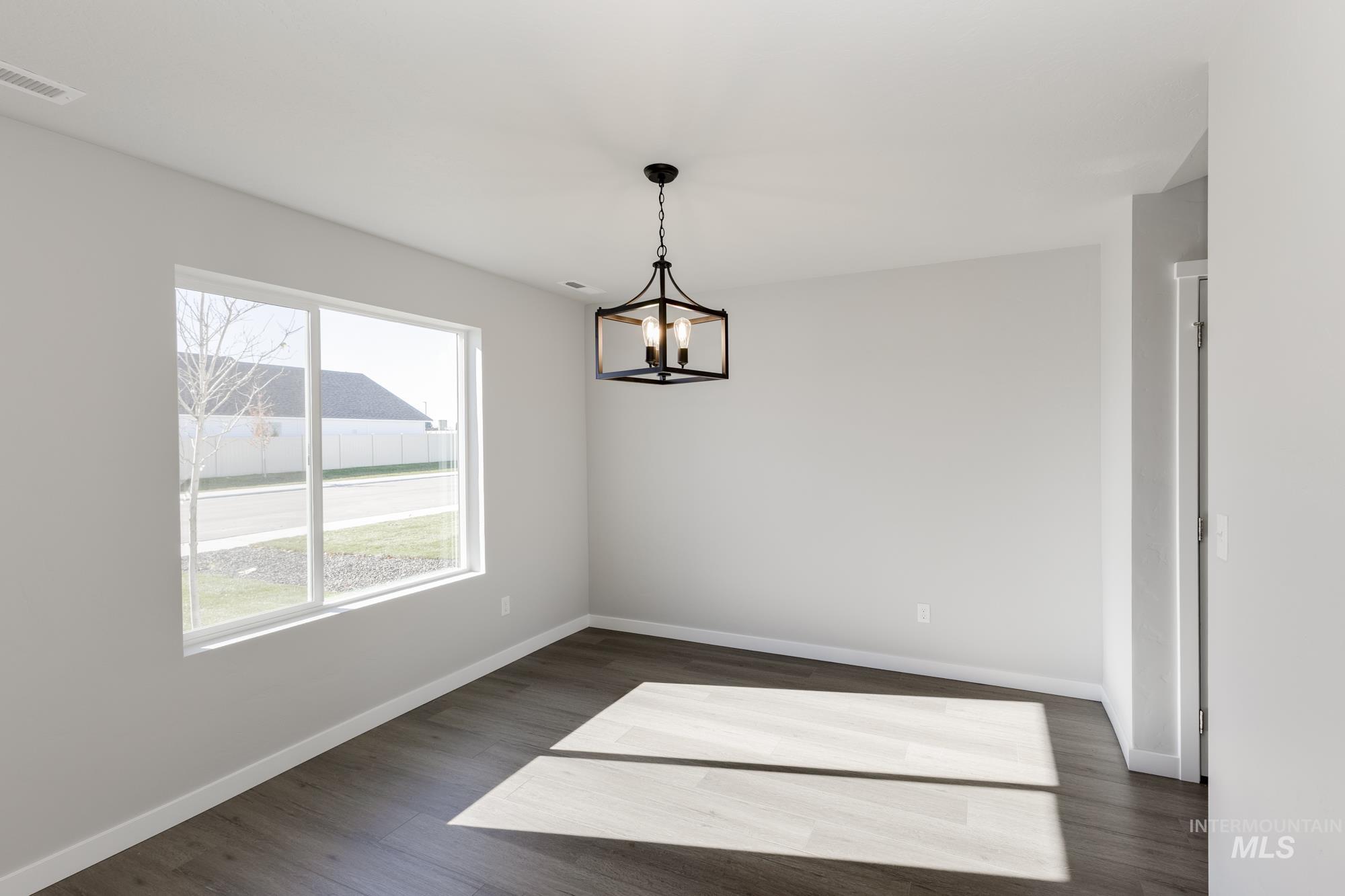 Empty room with dark wood-type flooring and a chandelier