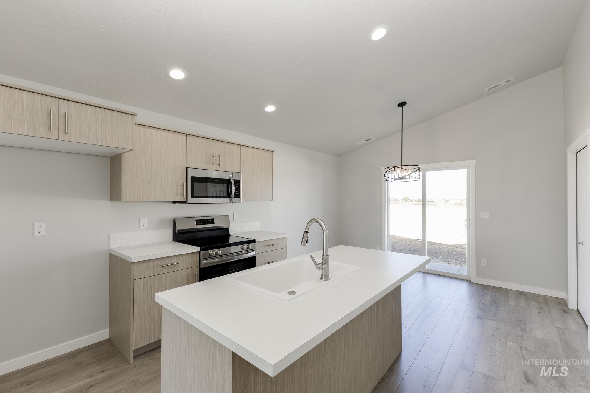 Kitchen with stainless steel appliances, light countertops, light brown cabinets, vaulted ceiling, and light wood-style floors