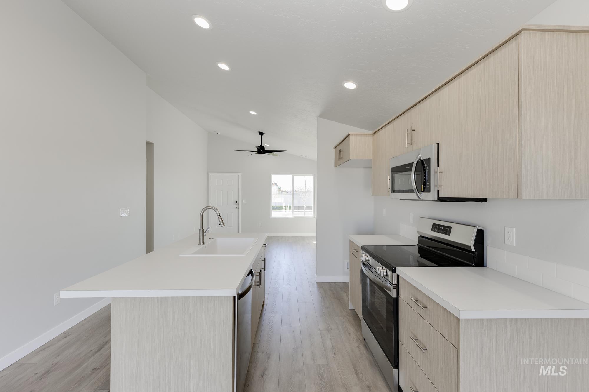 Kitchen with light brown cabinets, appliances with stainless steel finishes, light countertops, modern cabinets, and lofted ceiling