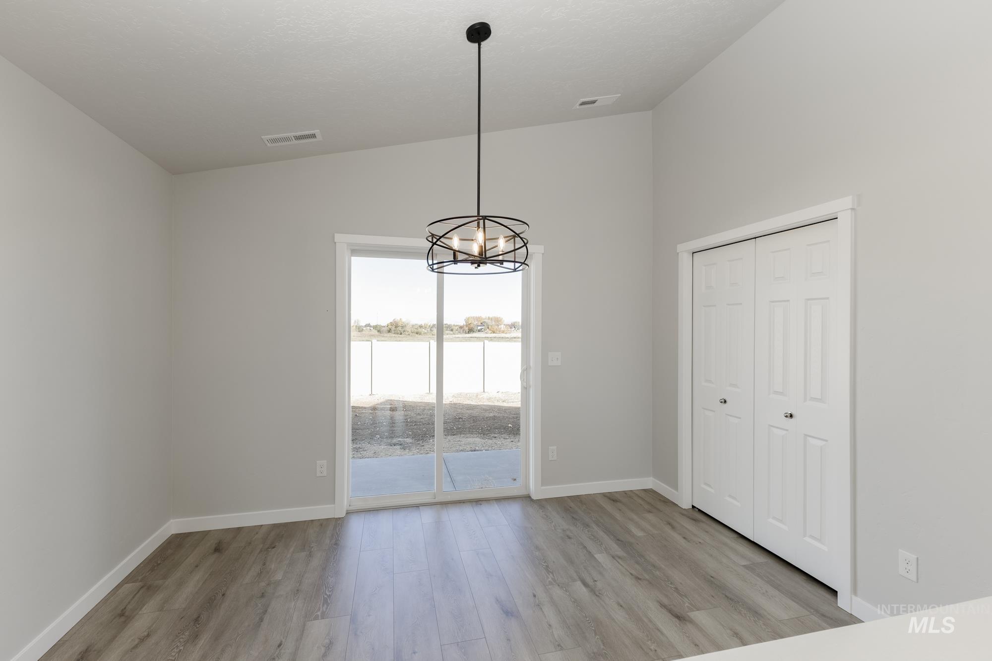 Unfurnished dining area featuring vaulted ceiling, a chandelier, light wood finished floors, and a water view