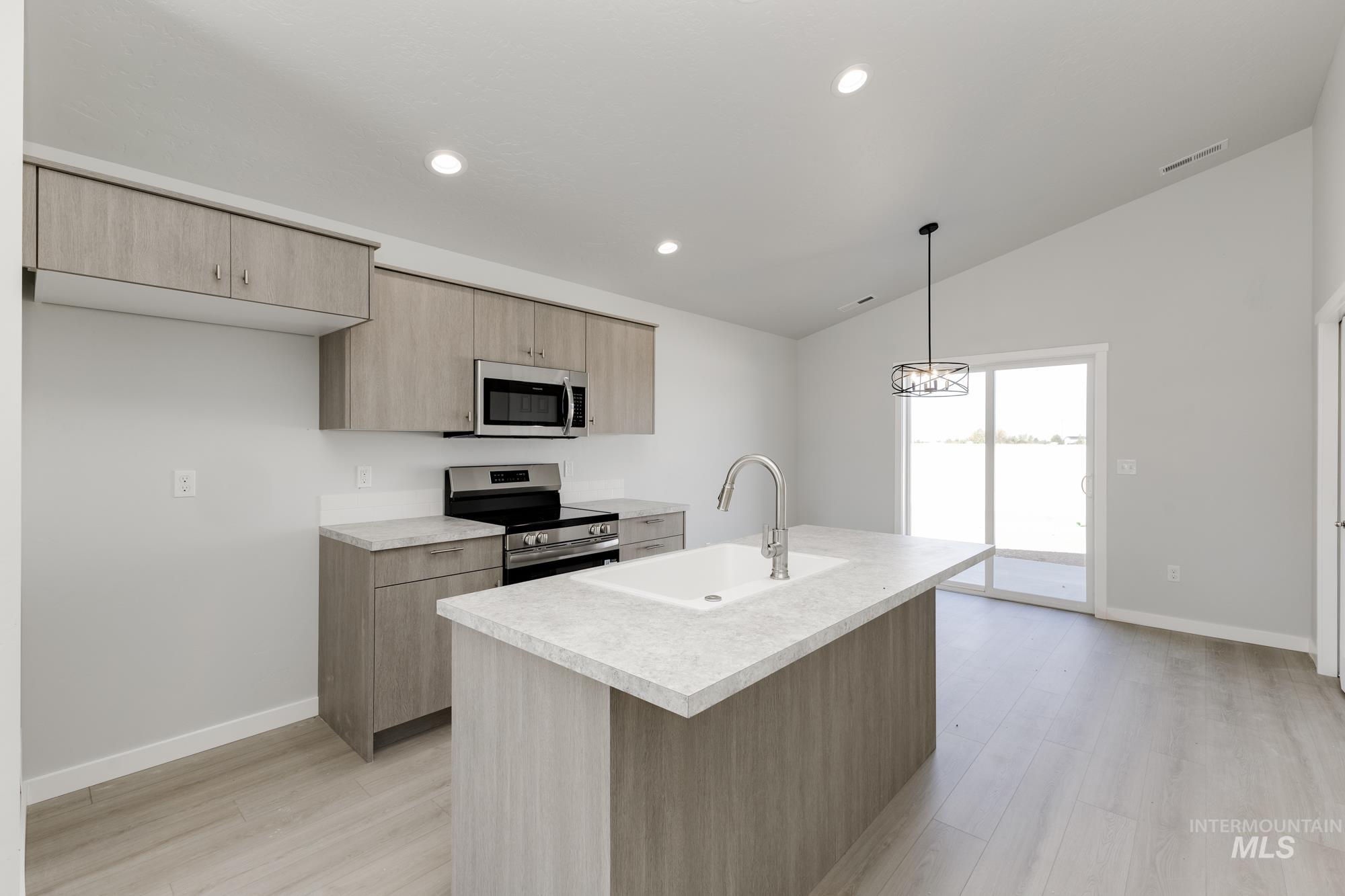Kitchen with stainless steel appliances, light brown cabinets, light countertops, lofted ceiling, and recessed lighting